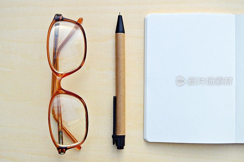 一副眼镜的水平照片，一支钢笔和一张白色的笔记本，放在一个木制的米色水平背景上，很有美感。