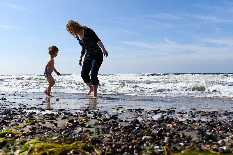 一个快乐的母亲和儿子在海滩上玩的后视图。