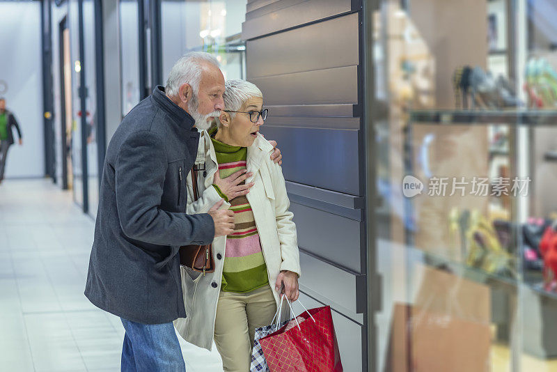 快乐的成熟夫妇提着购物袋在购物中心和站在商店的橱窗附近