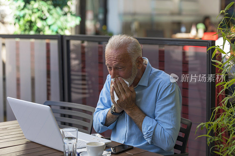 一个老人在餐厅花园用纸巾擤鼻子