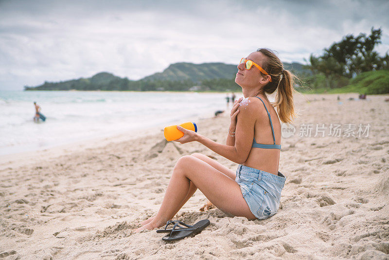 夏日——年轻女子在海滩上涂抹防晒霜，保护皮肤