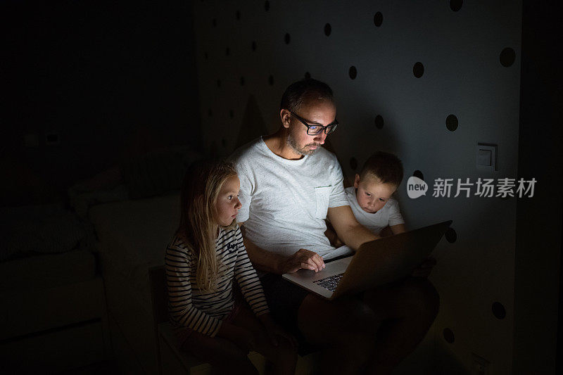父亲和孩子们坐在卧室里，使用笔记本电脑。