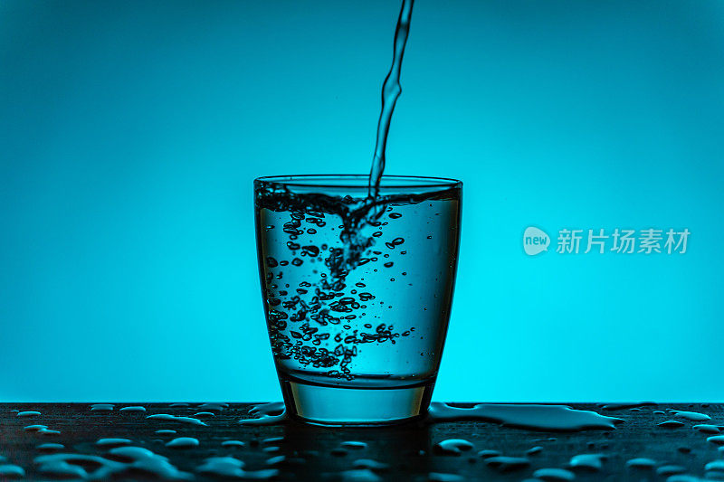 水从水瓶流入玻璃杯-蓝色的背景