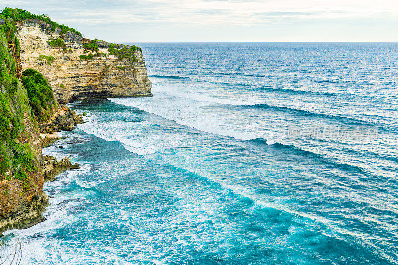 Uluwatu巴厘岛。蓝色的海洋和岩石山，覆盖着热带树木。