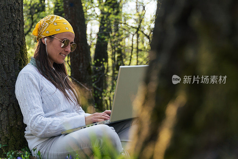 一个嬉皮女人在大自然中摆弄着笔记本电脑。