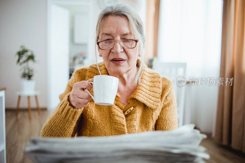 一位老妇人在家里看报纸，喝咖啡