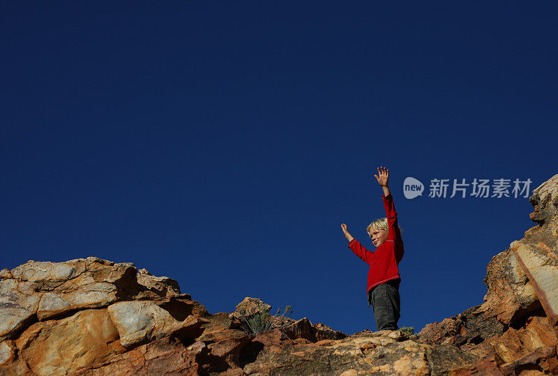 一个小男孩通过举起双手来庆祝爬上一块巨石。