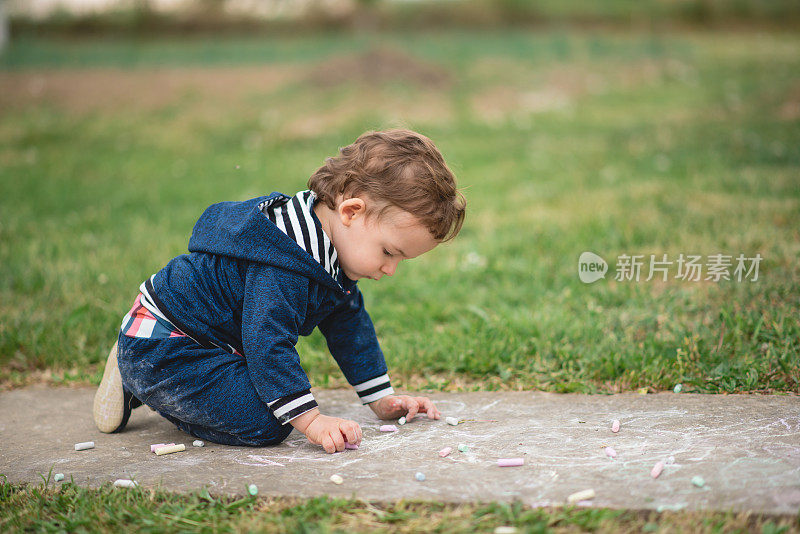 小男孩在户外玩，坐在地上用粉笔画画