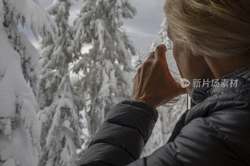 女人喝着水，望着窗外白雪覆盖的树木