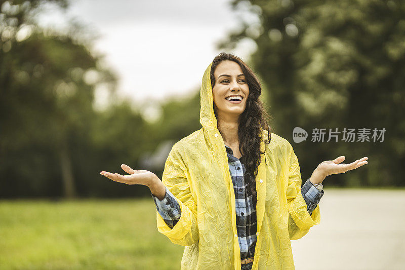 快乐的年轻女子穿着黄色雨衣，享受着雨