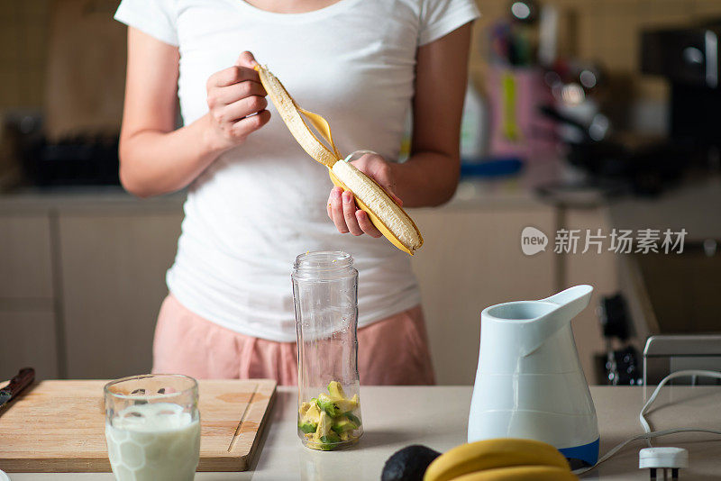 一个女人正在切香蕉，准备做鳄梨和香蕉冰沙作为健康的早餐饮料