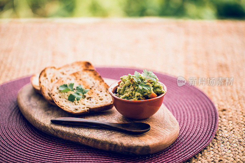 一碗鳄梨色拉酱和无谷蛋白面包放在木砧板上