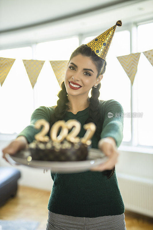 一名年轻女子在家庆祝圣诞节，手里拿着巧克力蛋糕，蛋糕上插着2021年的蜡烛