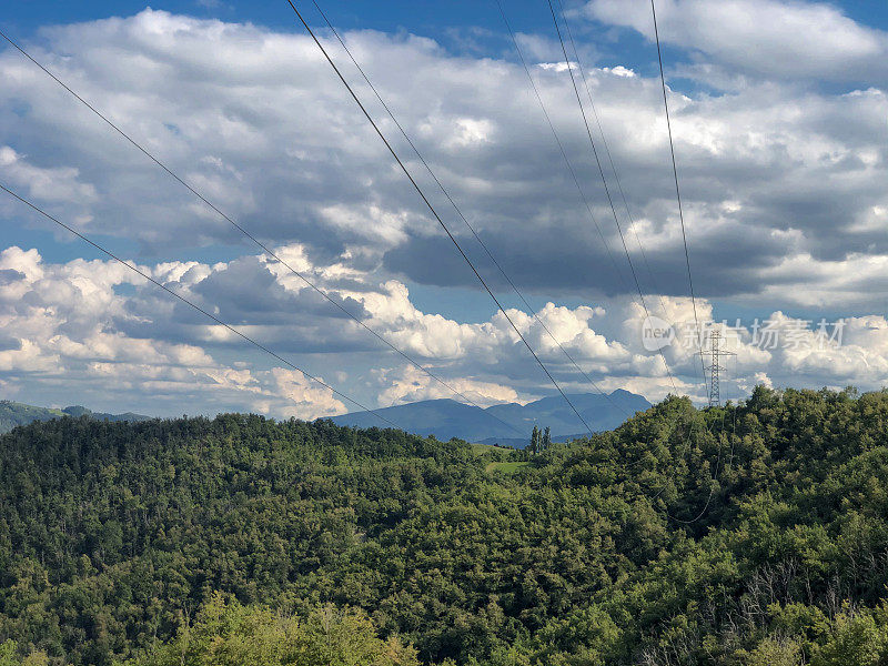电力基础设施。电线横跨山川景观、蓝天、绿色田野和小路。能源产业。本空间