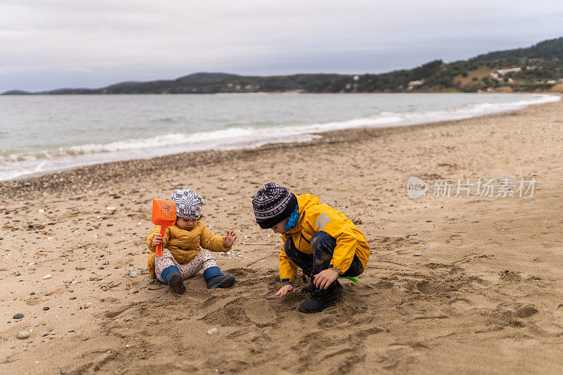 弟弟和妹妹在寒冷的日子里在海滩上玩塑料玩具