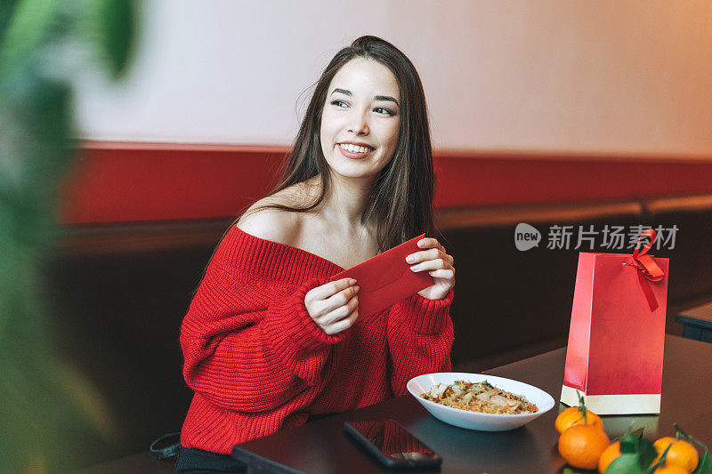 美丽年轻的亚洲女子在餐厅吃亚洲食物与红包庆祝中国新年