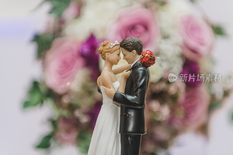 浪漫的新娘和新郎在蛋糕上跳舞，在一束粉红色，白色和紫色的玫瑰前