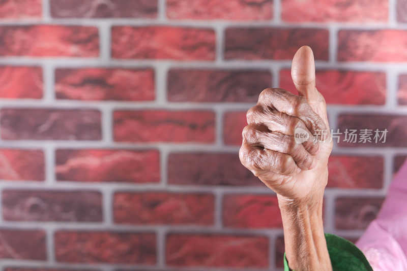 年长的女性举起大拇指，顶着墙