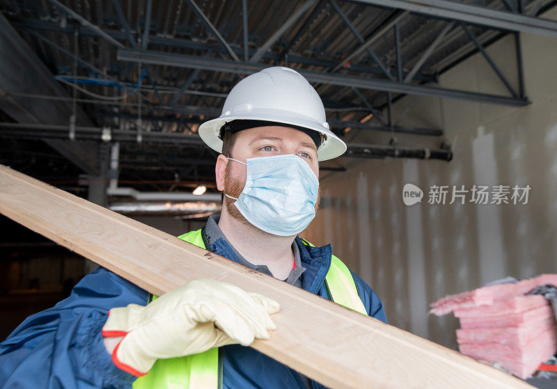 建筑工人或工程师在工地上搬运材料并查看剪贴板上的平面图