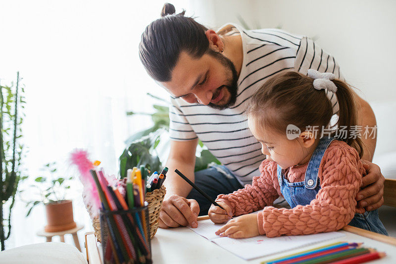 快乐的父亲帮助女儿做作业。小女孩在家里做作业。