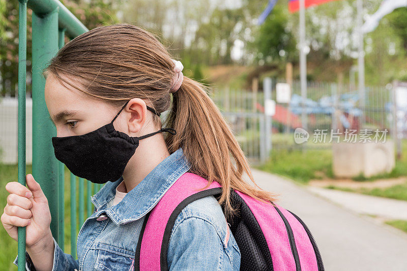 一名戴着口罩的女学生在校门外等待新冠肺炎疫情封锁后重新开放