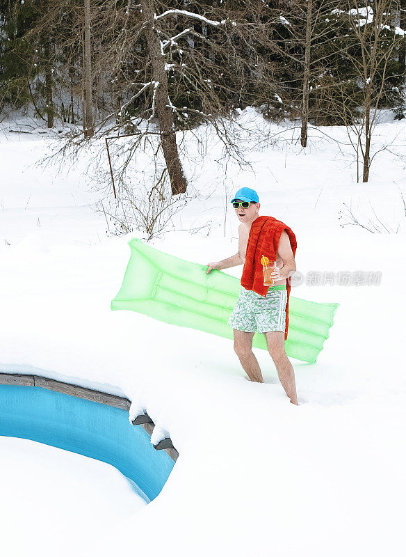 一个年轻人站在泳裤和气垫在他的手。一名男子站在积雪覆盖的室外游泳池旁。