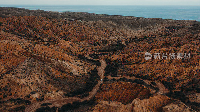 一辆汽车在吉尔吉斯斯坦美丽的橙色峡谷弯道上行驶的鸟瞰图