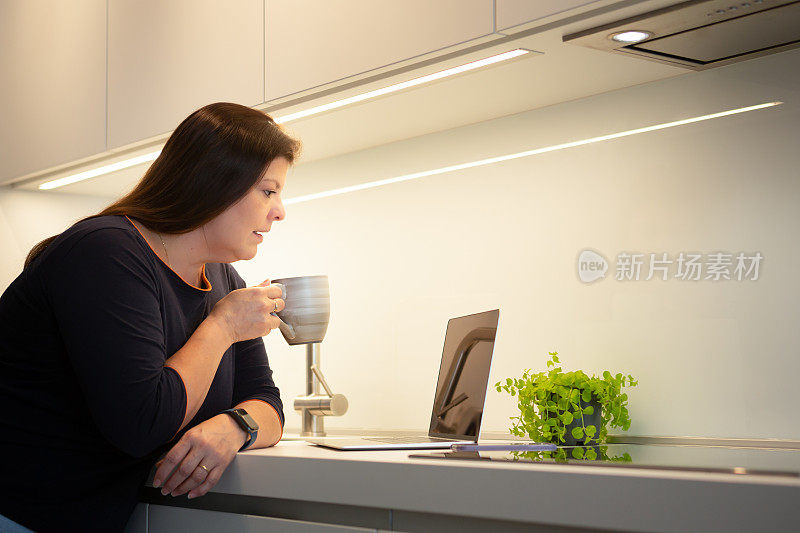 女士正在厨房里喝咖啡，同时与在家工作的科技互动