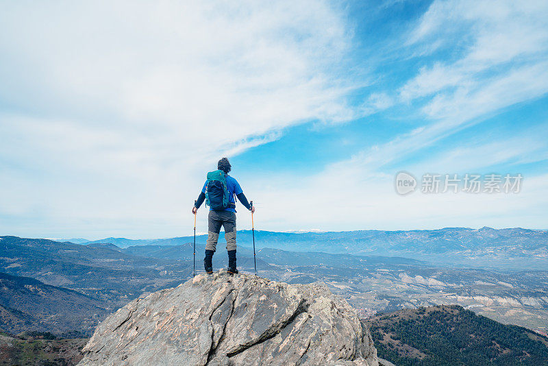 背景摄影师登山运动员是看风景，而持有登山杆在一个岩石山的顶峰。