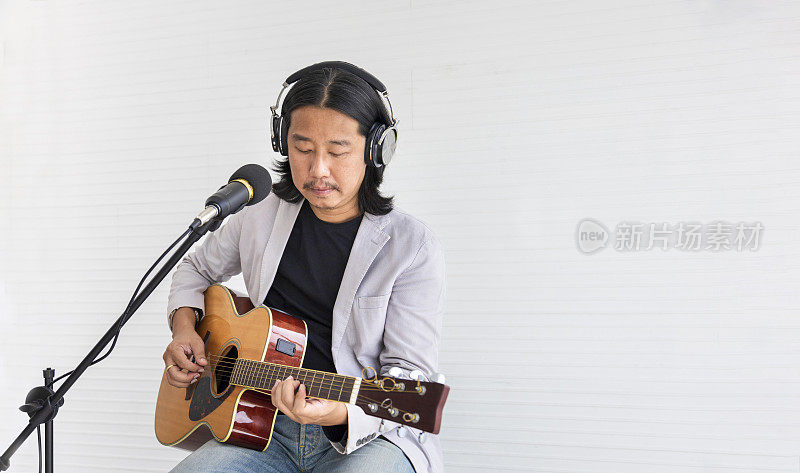 亚洲艺术家在白色背景下演唱歌曲和演奏原声吉他，为现场声学音乐会和音乐相关概念