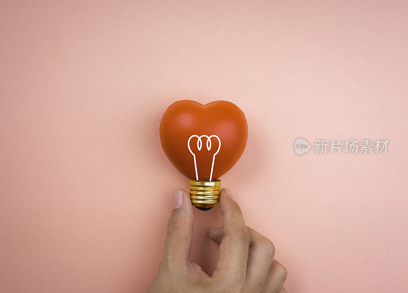 手握灯泡图标符号红心球上粉红色柔和的背景，最小的风格。爱，关心，分享，给予，幸福，灵感和想法概念。