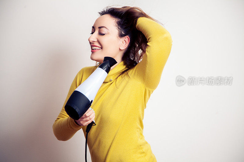 年轻微笑的女人用吹风机把头发卷起来