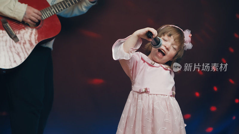 穿着复古礼服的小女孩在舞台上唱歌，她的父亲弹着原声吉他