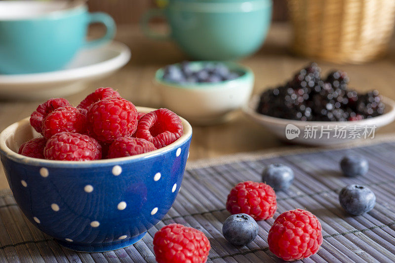 蓝碗里的Rapsberries放在桌子上，装饰有蓝莓和黑莓