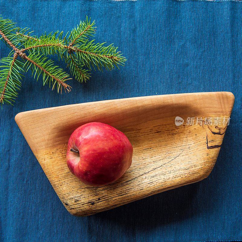 不对称木板上的红苹果和蓝色布上的小云杉枝的俯视图
