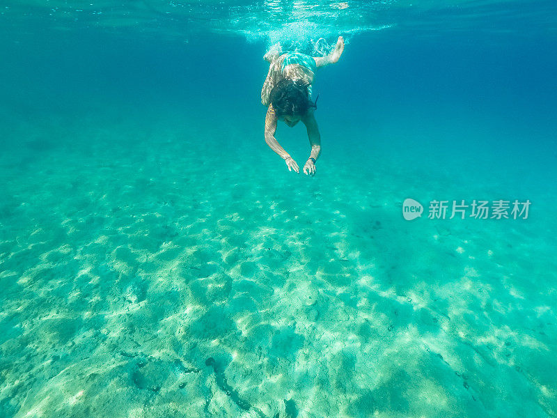 年轻女子在翠绿色的水下潜水，用防水相机拍摄