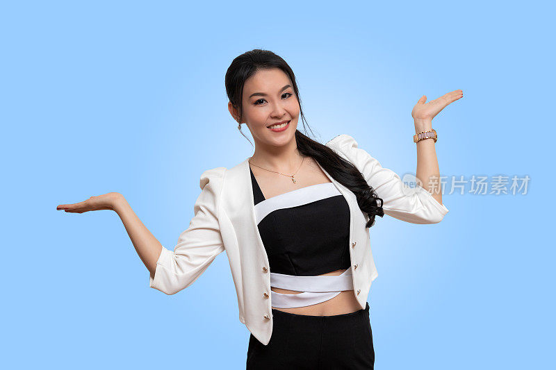 微笑美丽的亚洲女人与她的空手掌延伸到侧面呈现复制空间孤立在浅蓝色的背景。