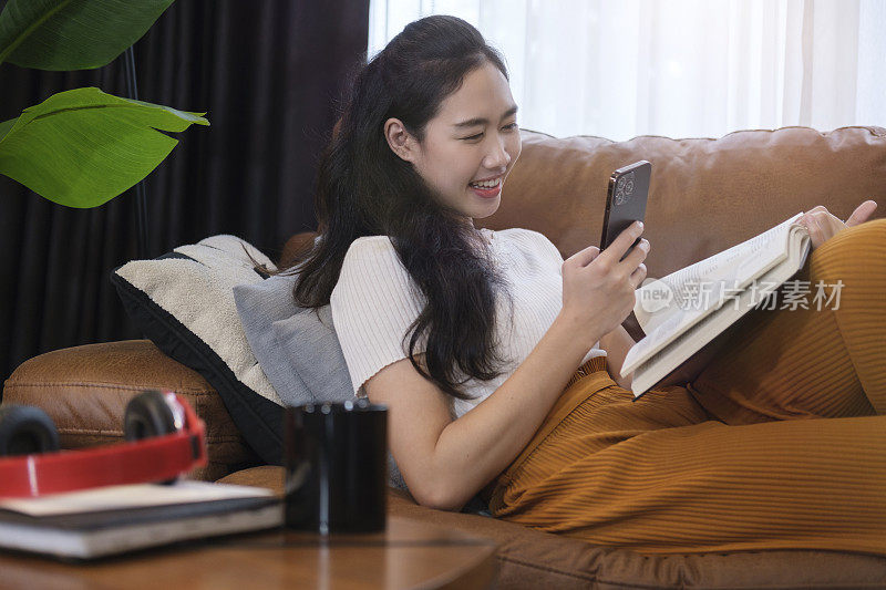 微笑的亚洲女人穿着休闲装在沙发上放松和使用手机。