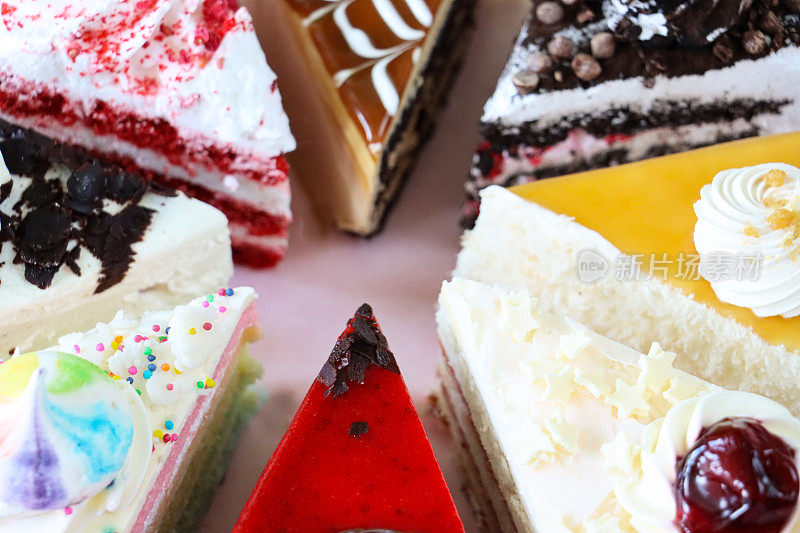 全帧图像的蛋糕品种切片圆防油羊皮纸，巧克力和樱桃蛋糕，黑森林蛋糕，红色天鹅绒，彩虹蛋糕，咖啡和大理石蛋糕，粉色背景，重点在前景，高架视图