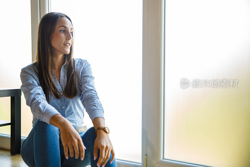 微笑的年轻女子坐在窗台上，看着外面，沉思