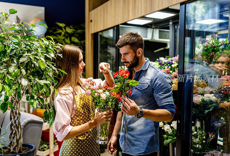 一家花店的女店员正在帮一个年轻人买花。