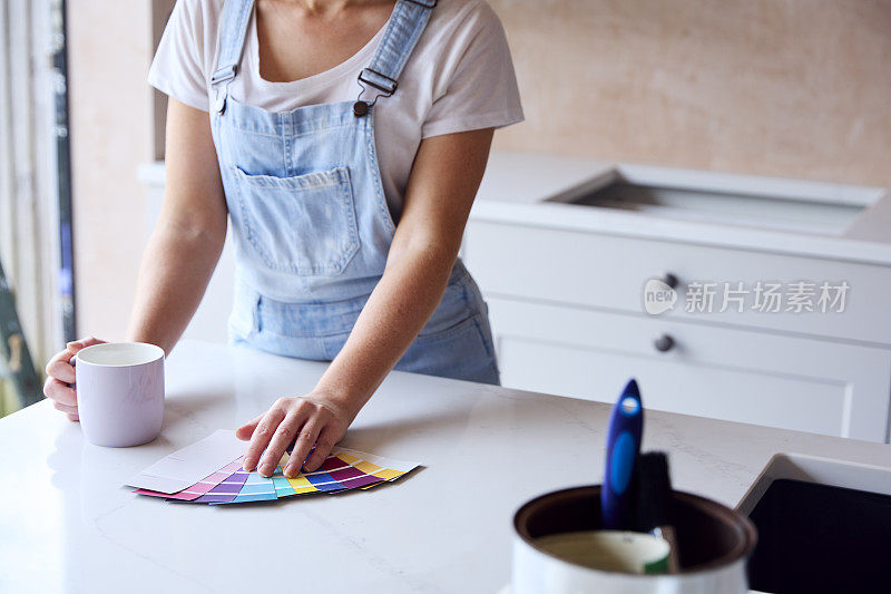 一个女人在家装修厨房的特写，她在喝咖啡休息时看着油漆色板