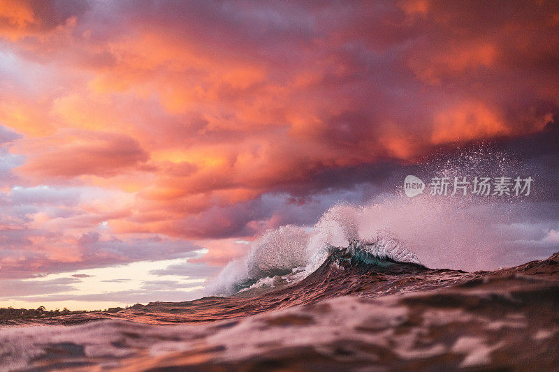 日落时分，在粉红色和金色的天空下，海浪碰撞出独特的水面图案