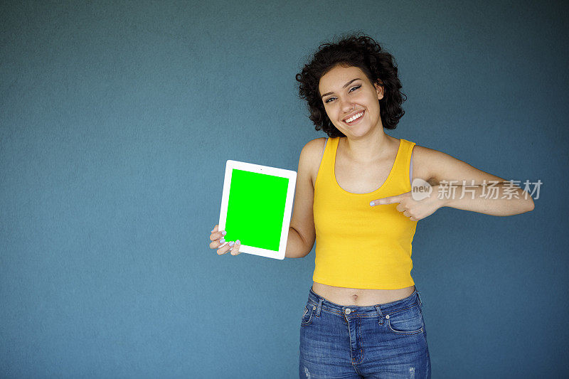 年轻女子指着蓝色背景下绿色屏幕的数字平板电脑
