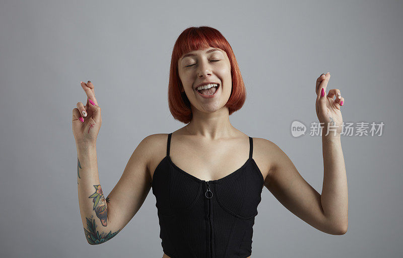 一位红短发的年轻女子微笑着，用手指做着许愿的手势。
