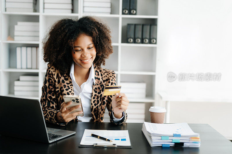 非洲妇女使用智能手机进行移动支付，网上购物，全渠道，坐在桌子上，虚拟图标图形界面屏幕