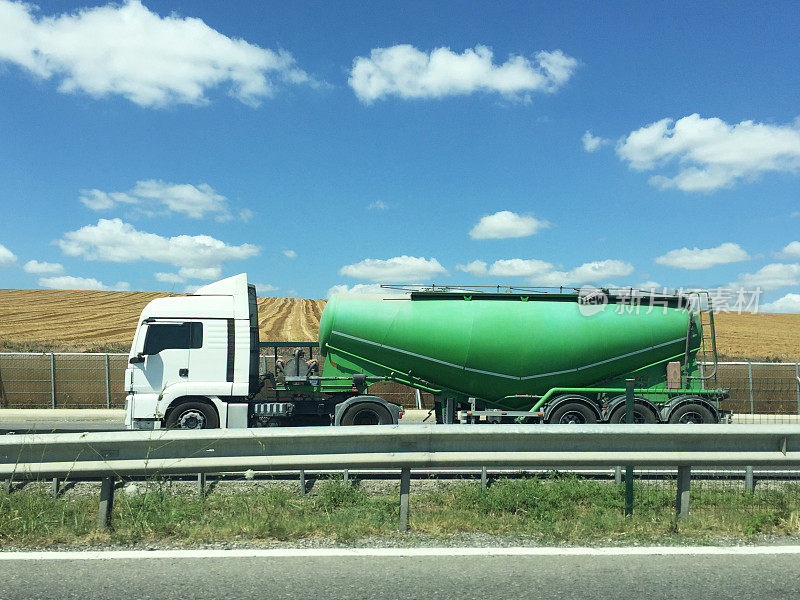 绿色的油罐车行驶在以农田和天空为背景的路上