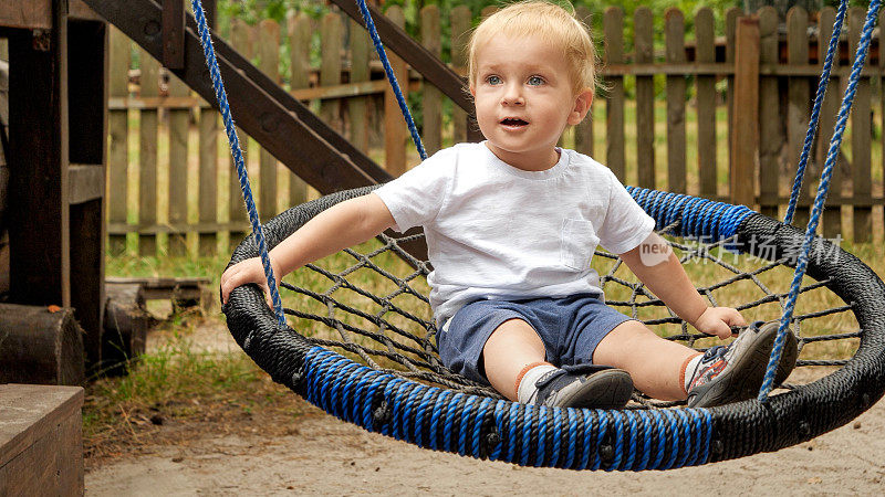 小男孩在公园里玩绳巢秋千时开心而微笑。孩子们在户外玩耍，孩子们玩得开心，暑假