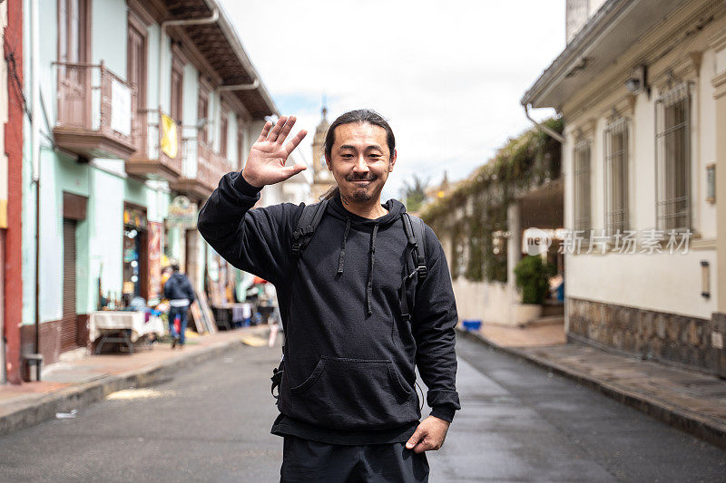 在哥伦比亚波哥大的历史街区，一名成熟的亚洲男子向镜头挥手