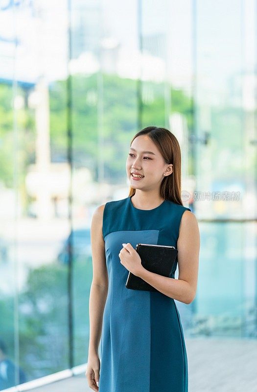 年轻的亚洲女子手持数码平板电脑，微笑着把目光移开